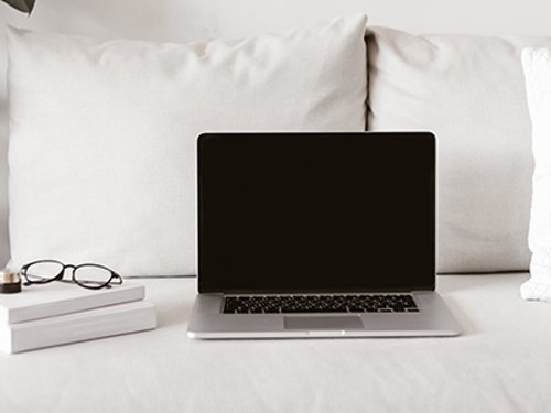 Laptop And Books On Sofa Modern laptop with blank display and stack of books with glasses lying on comfortable couch in stylish room