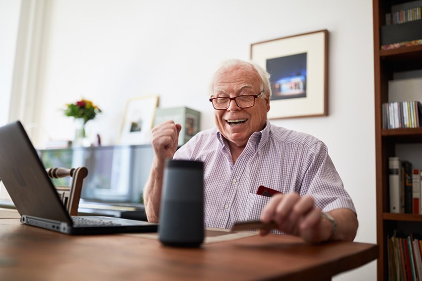 Senior man doing online shopping using a credit card, laptop and smart speaker device.